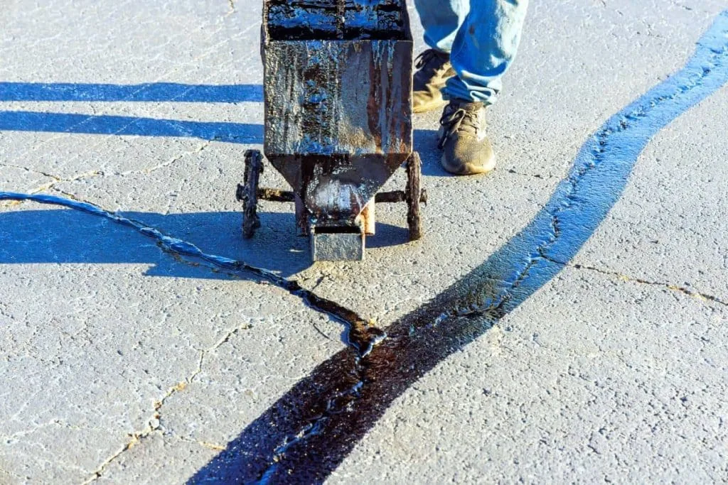 person sealing cracks in pavement